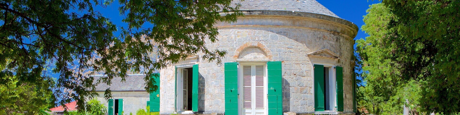 A stone building with a conical roof, green shutters, and a pathway leading to it.