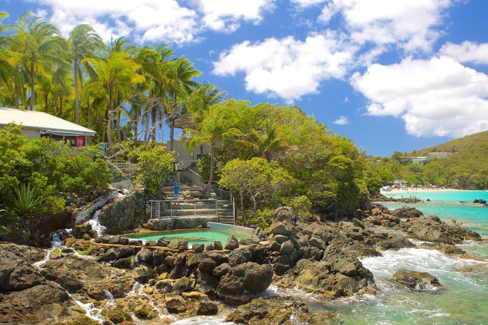 A tropical beach with clear turquoise waters, rocky shoreline, palm trees, and a small waterfall.