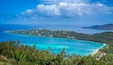A coastal landscape with turquoise waters, a small island with buildings, and a clear sky.