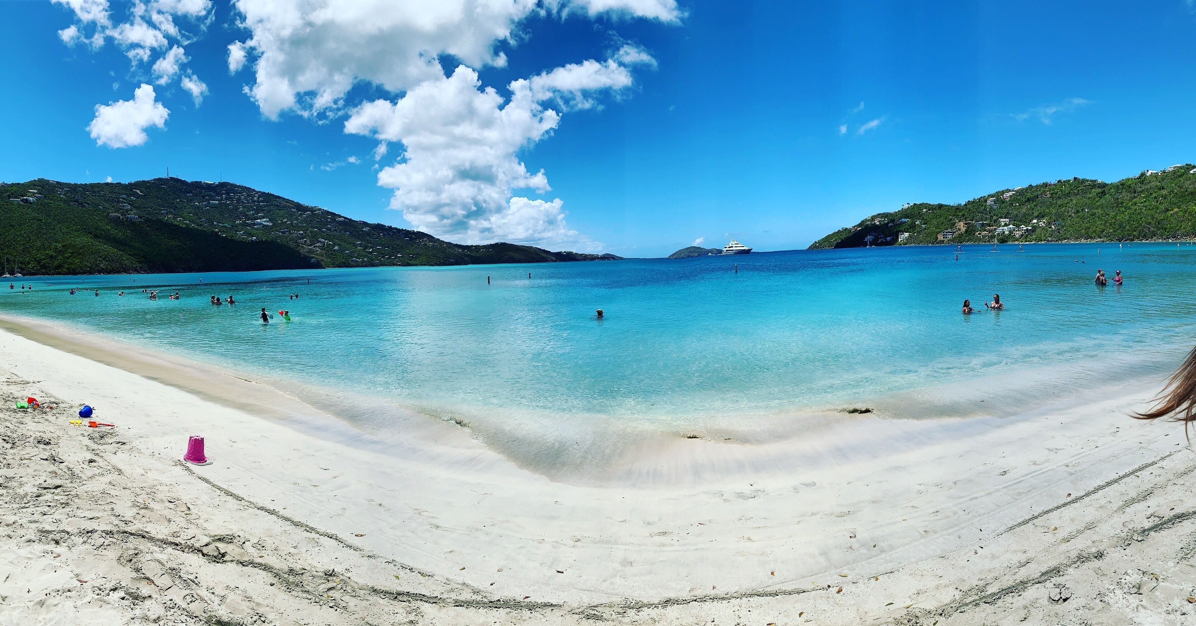 A beach with clear turquoise water, a sandy shore, and distant hills.