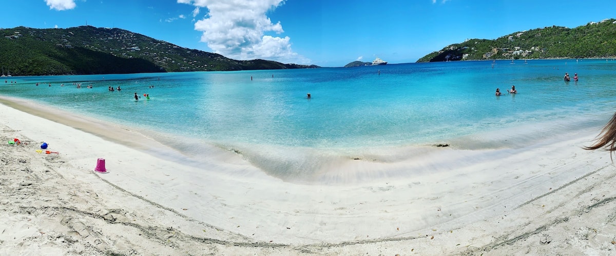 A beach with clear turquoise water, a sandy shore, and distant hills.