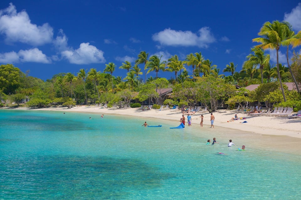 Uma praia tropical com águas turquesa cristalinas, palmeiras e pessoas na praia.