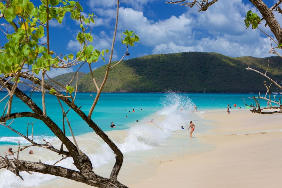 A beach with turquoise water, people swimming, and a mountain in the background.