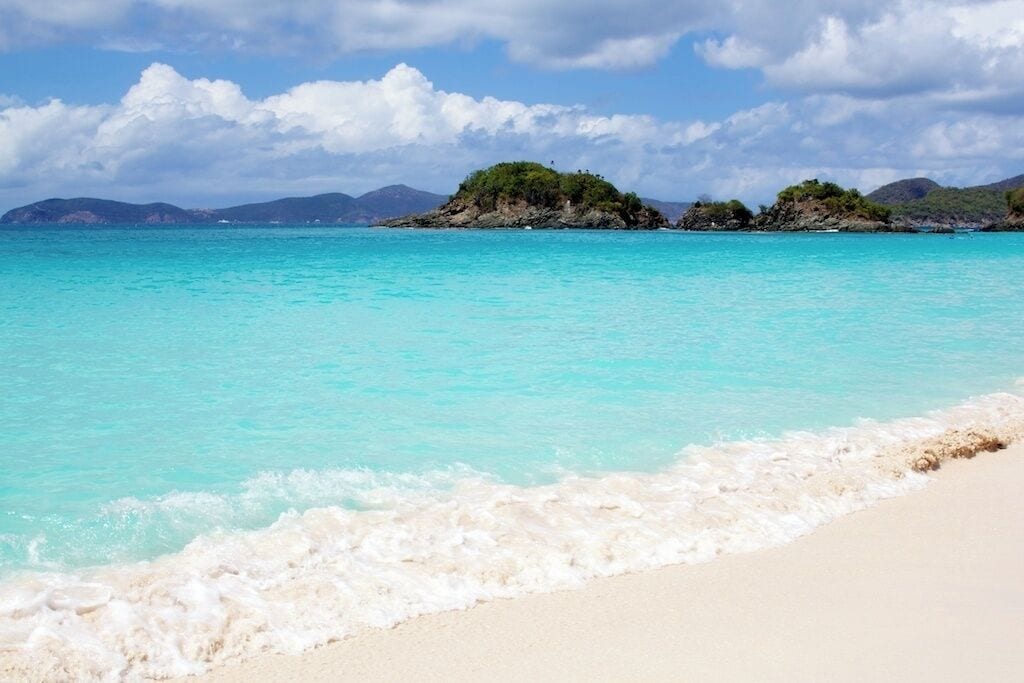 A turquoise sea with white sand beaches and small green islands in the distance.