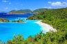A tropical beach with clear turquoise waters, lush greenery, and distant mountains.