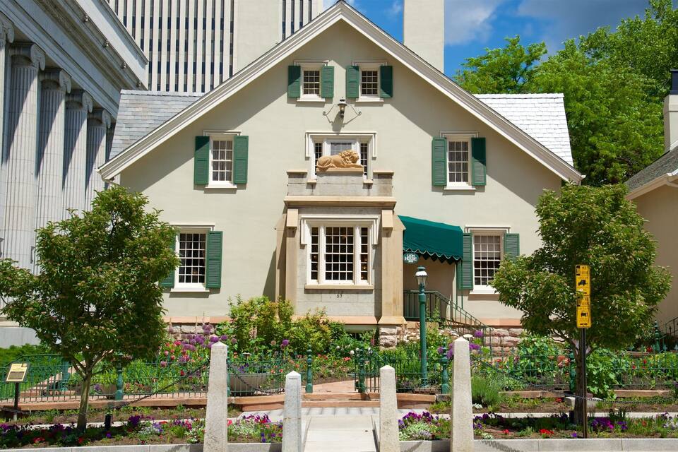 A historic building with green shutters, a lion statue, and a well-maintained garden with colorful flowers.