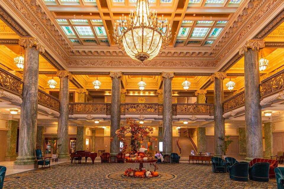 A grand lobby with ornate chandeliers, marble columns, and a central floral arrangement.