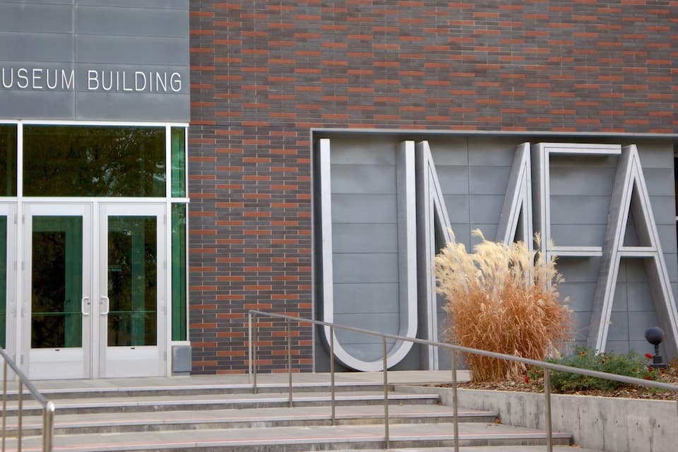 The entrance to the Ice Museum Building with a glass facade, a brick wall, and a large 'UMA' sign.