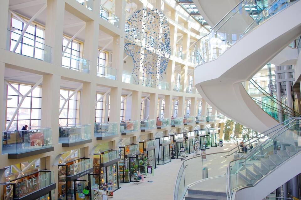 Un centro comercial de varios niveles con barandillas de vidrio, escaleras mecánicas y diversas tiendas.