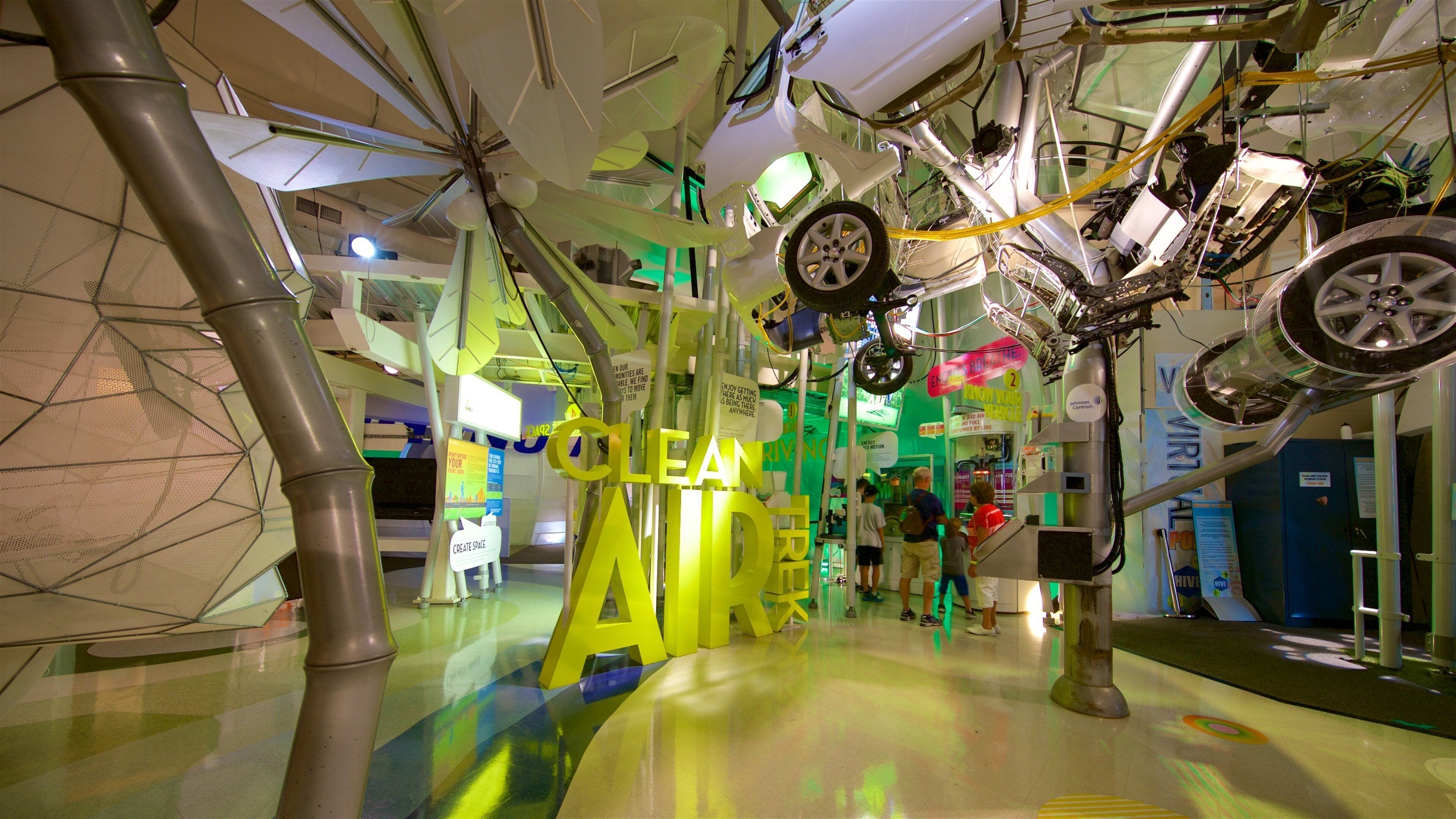 Mostra di auto con diversi veicoli sospesi in aria, un grande cartello giallo con la scritta 'CLEAN' e un cartello verde con 'ENJOY'.