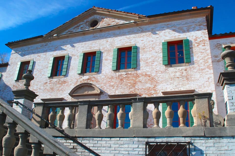 A historic building with white brick walls, green shutters, and a stone balustrade.