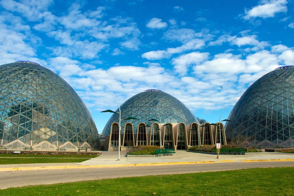 Three large geodesic domes with a clear blue sky and scattered clouds in the background.