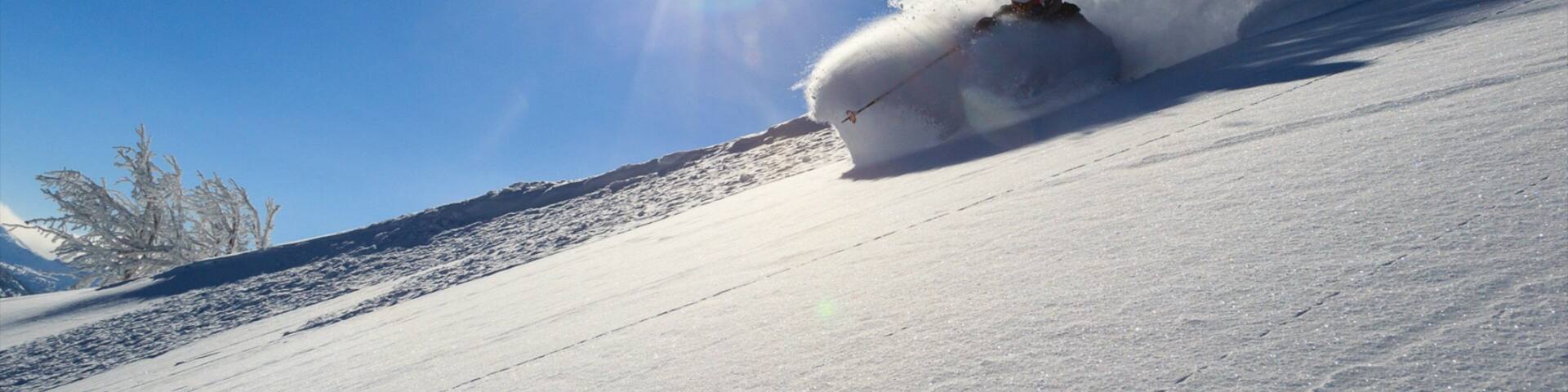 A skier carving a turn on a snowy slope under a clear blue sky.