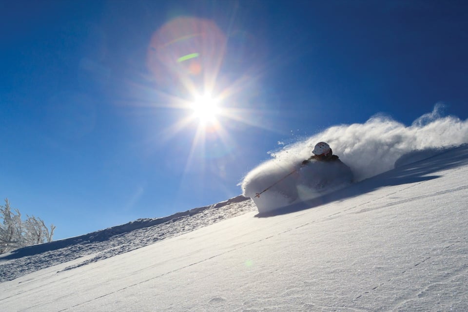 Uno sciatore che traccia una curva su un pendio innevato sotto un cielo azzurro limpido.