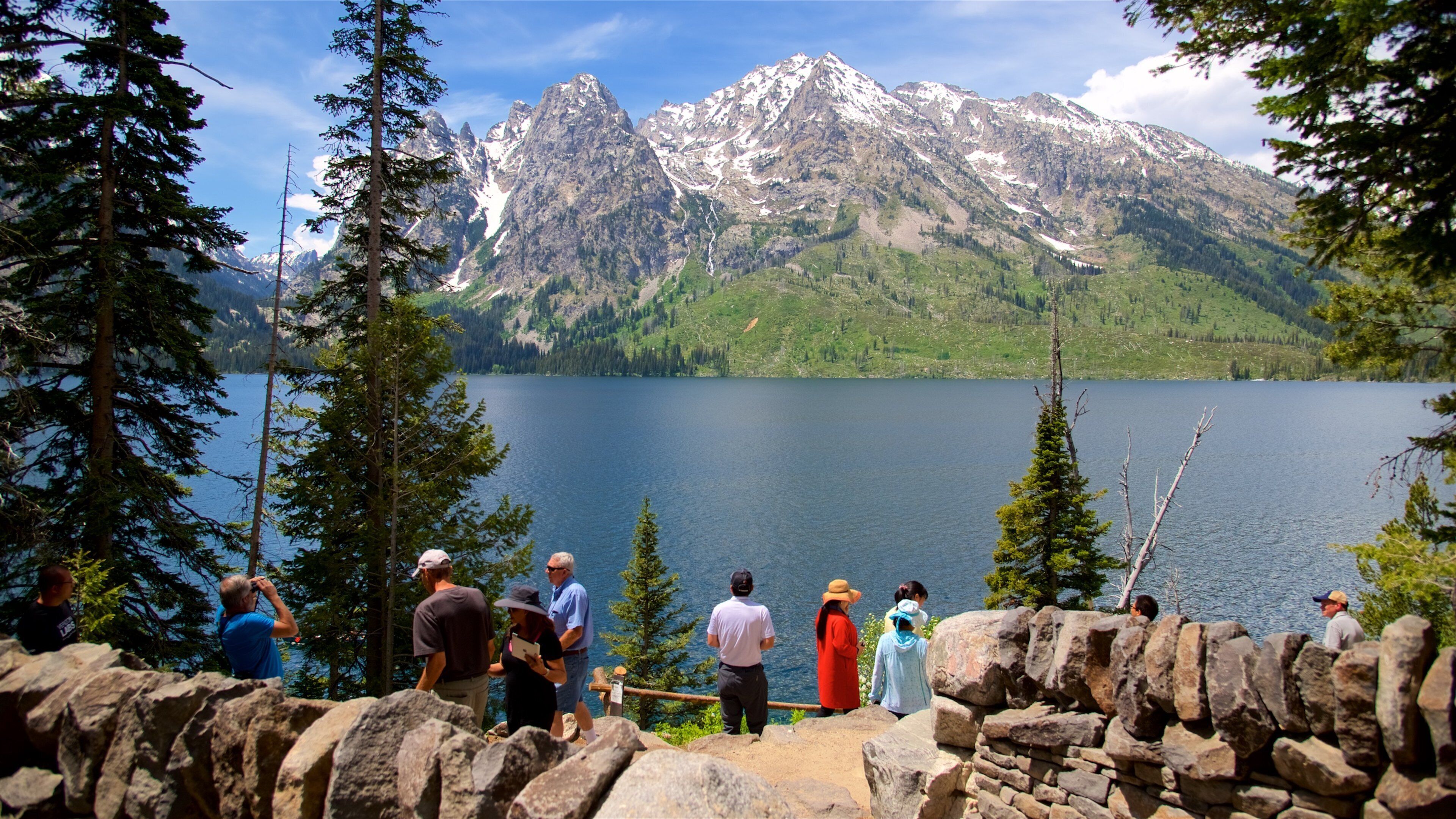 A group of people standing on a rocky ledge overlooking a lake with mountains in the background.