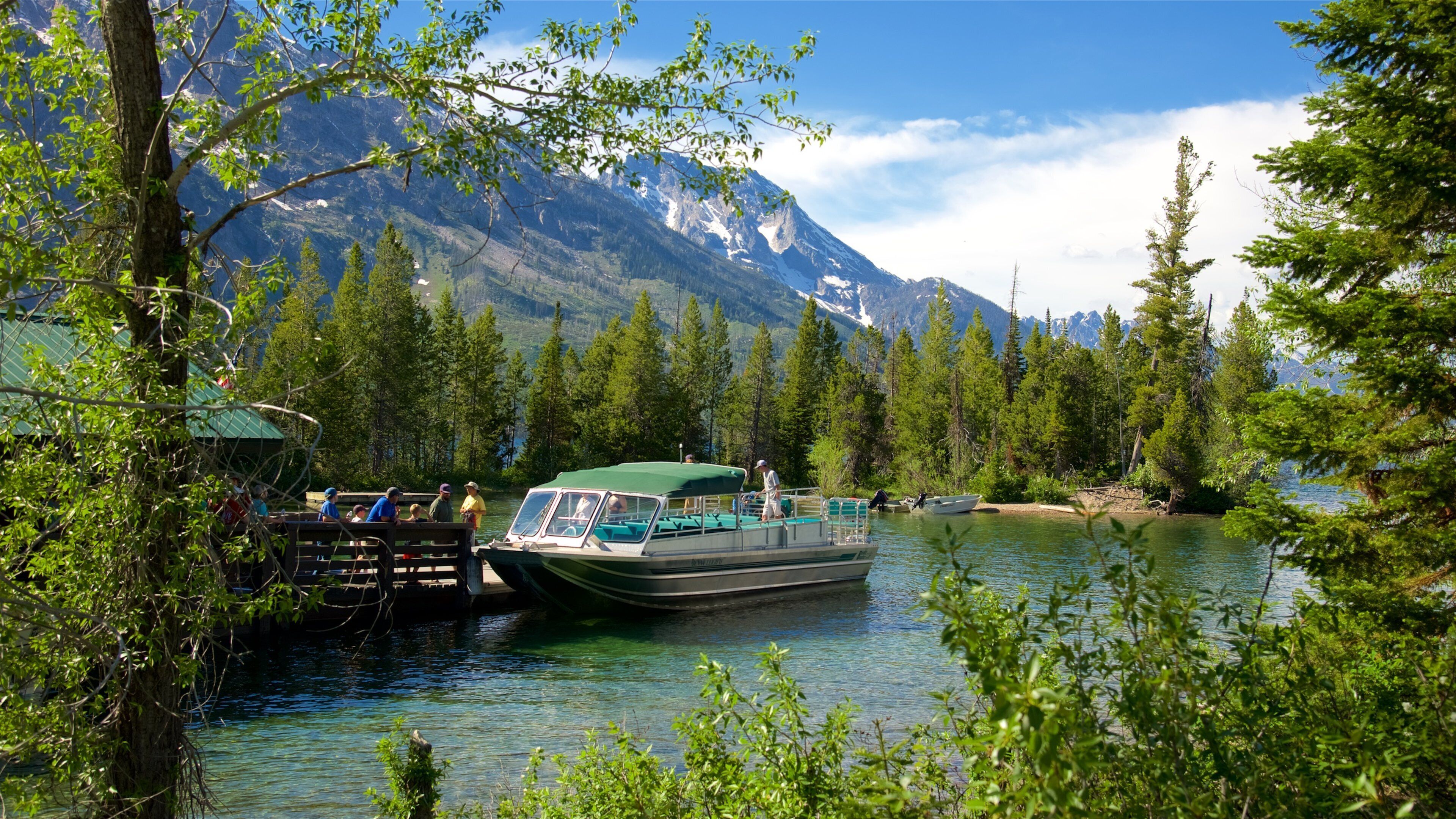 A boat docked at a pier surrounded by dense forest and mountains.