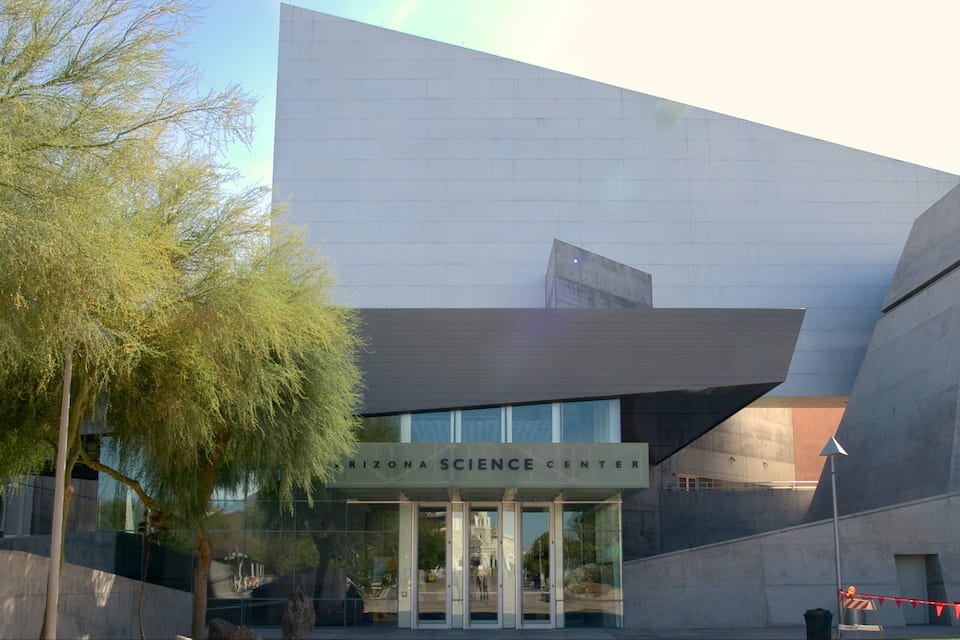 The exterior of the Reina Science Center with a modern architectural design, featuring a large glass entrance and a tree in the foreground.