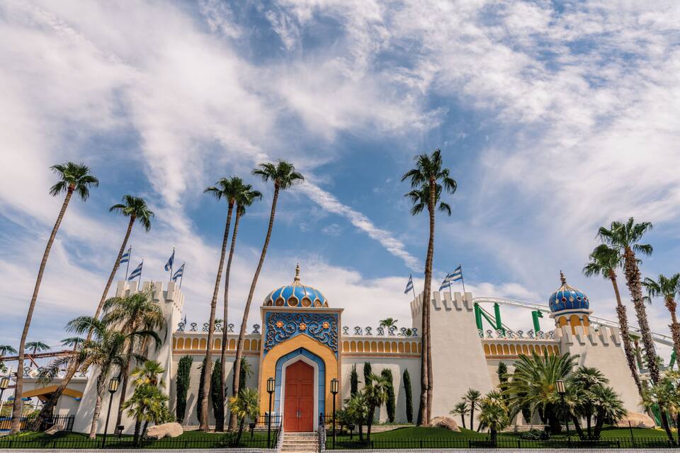 A large building with a red door and blue and orange domes, surrounded by palm trees.