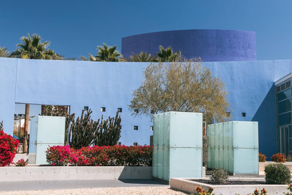 A modern building with a blue facade, surrounded by cacti and flowering plants.