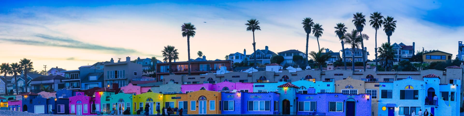 A coastal town with colorful buildings, palm trees, and a calm body of water reflecting the architecture.