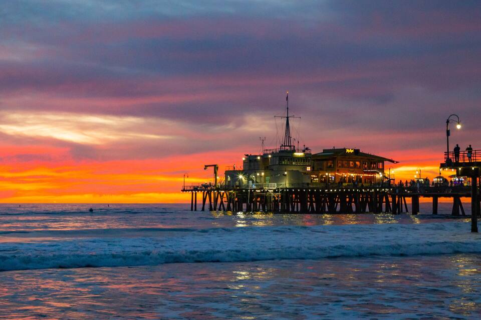 A pier at sunset with a building on it and the ocean in the foreground.