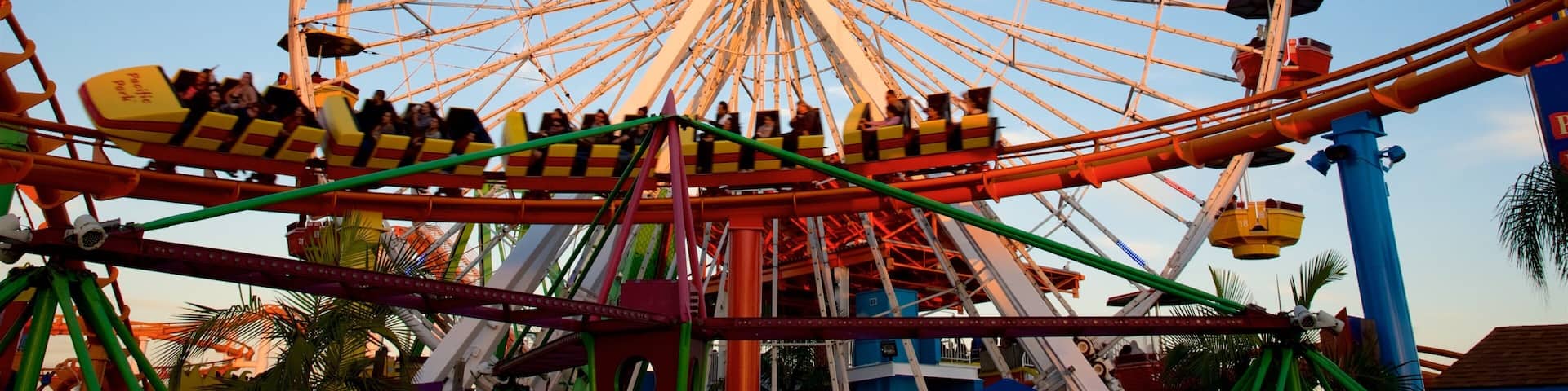 Une grande grande roue avec des cabines portant l’inscription « Pacific Park » et des montagnes russes au premier plan.