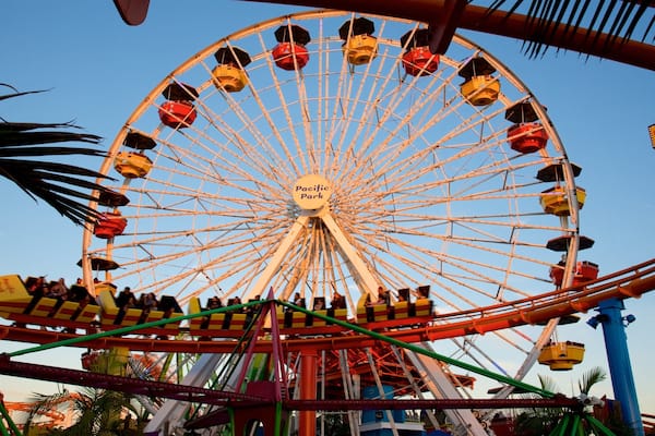 Une grande grande roue avec des cabines portant l’inscription « Pacific Park » et des montagnes russes au premier plan.