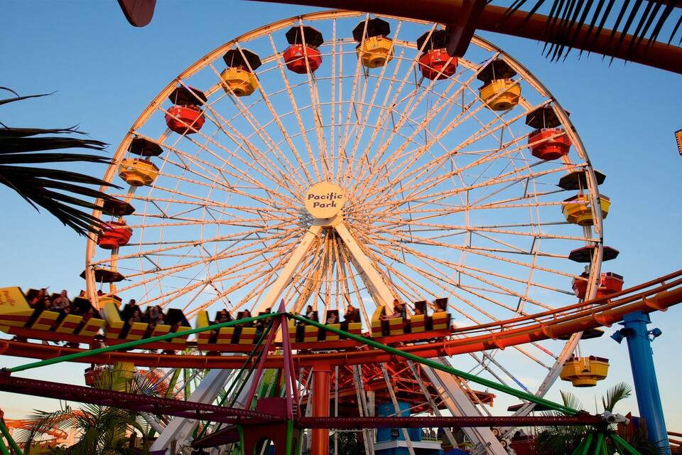 A large Ferris wheel with cabins labeled "Pacific Park" and a roller coaster in the foreground.