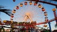A large Ferris wheel with cabins labeled "Pacific Park" and a roller coaster in the foreground.