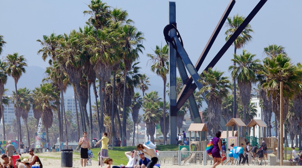 Venice Beach showcases vibrant activities under palm trees with an iconic sculpture in the background during a sunny day in California
