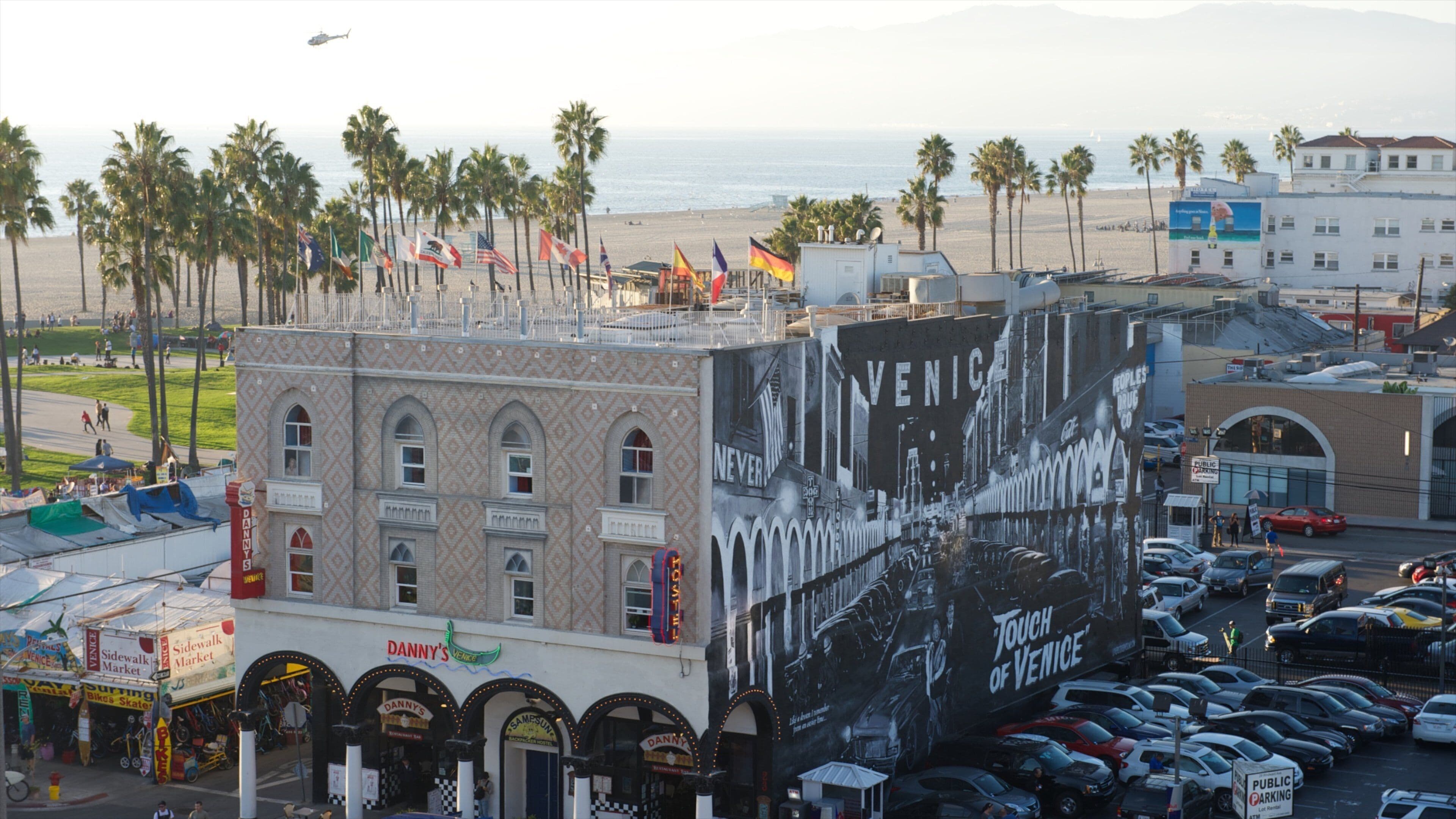 Un edificio con un mural grande de Venecia, una playa con palmeras y un estacionamiento concurrido.