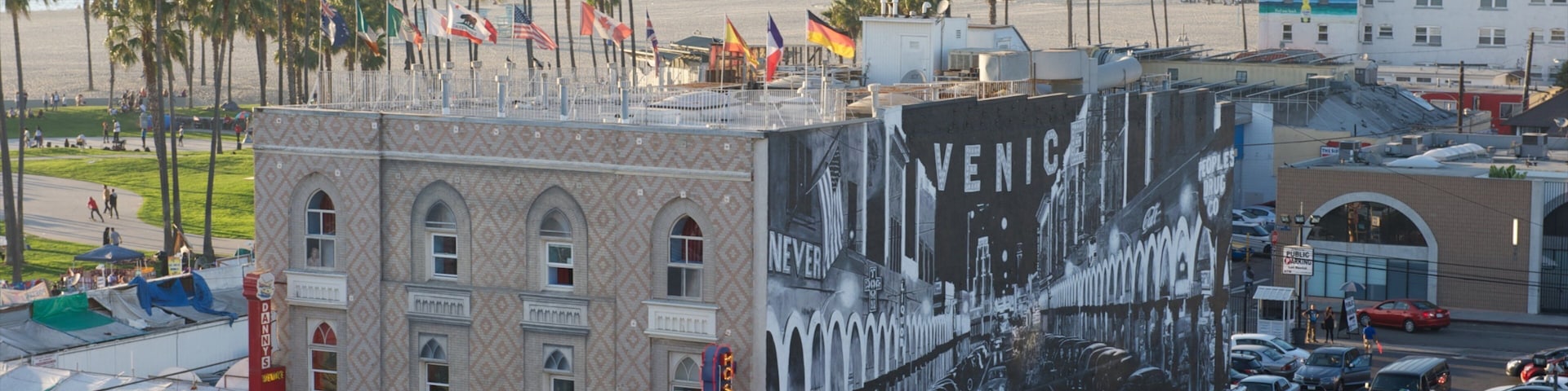 Un edificio con un mural grande de Venecia, una playa con palmeras y un estacionamiento concurrido.