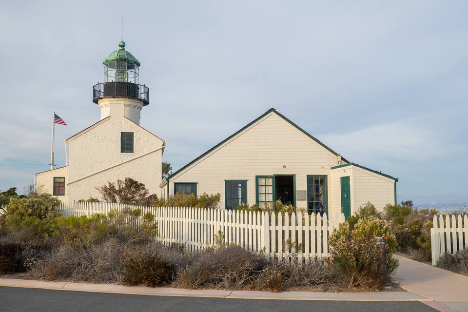 A lighthouse with a white picket fence, green shutters, and an American flag.