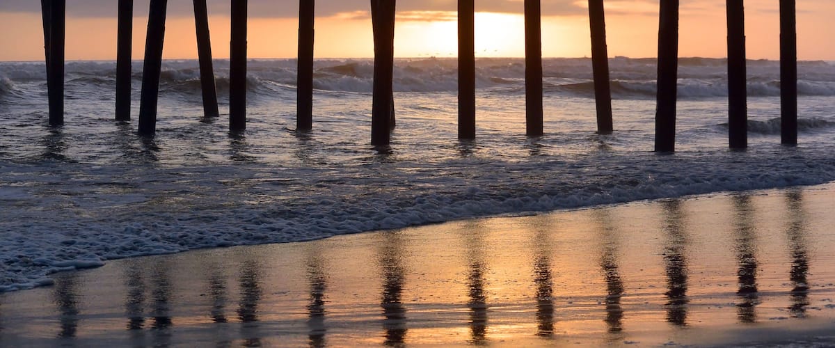 A beach with waves at sunset, wooden posts, and a reflective wet sand surface.
