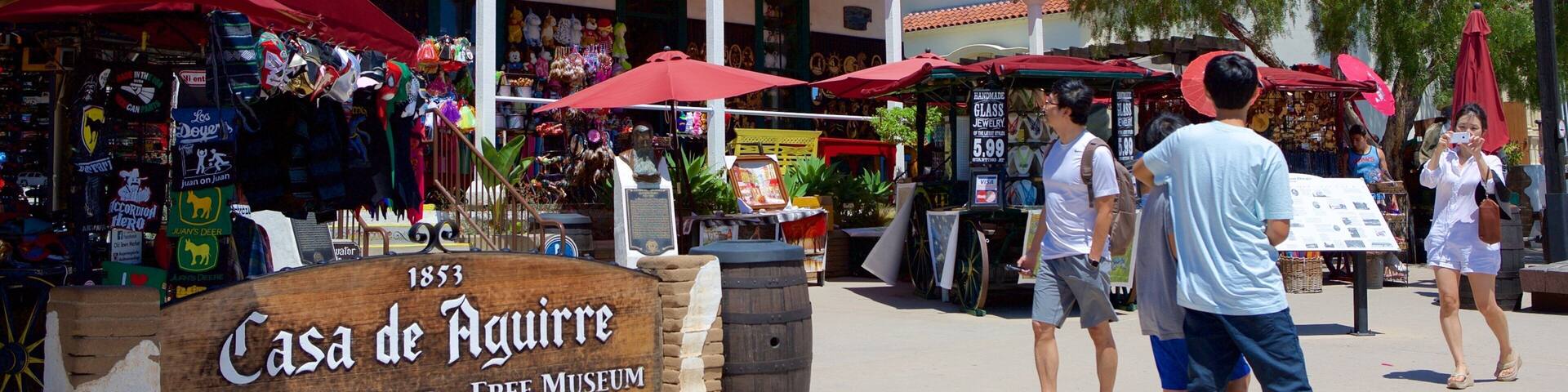 A bustling outdoor market with red umbrellas, a sign for Casa de Aguirre, and people walking around.