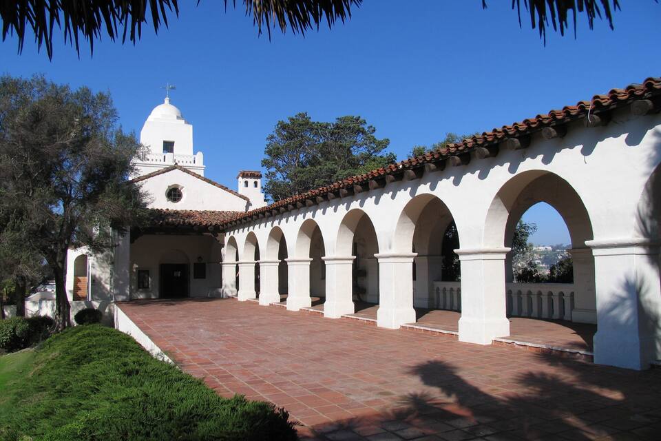 Um edifício branco com cúpula e arcos, rodeado por vegetação.