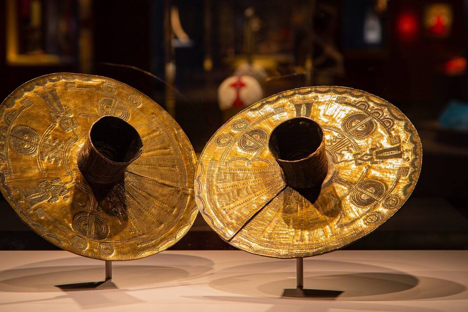 Two golden, intricately designed objects with circular openings, displayed on stands.