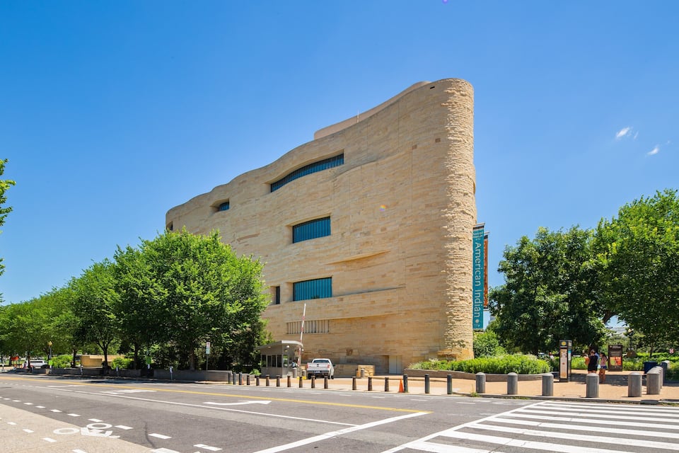 Un edificio moderno con fachada curva, rodeado de árboles y un paso de peatones.