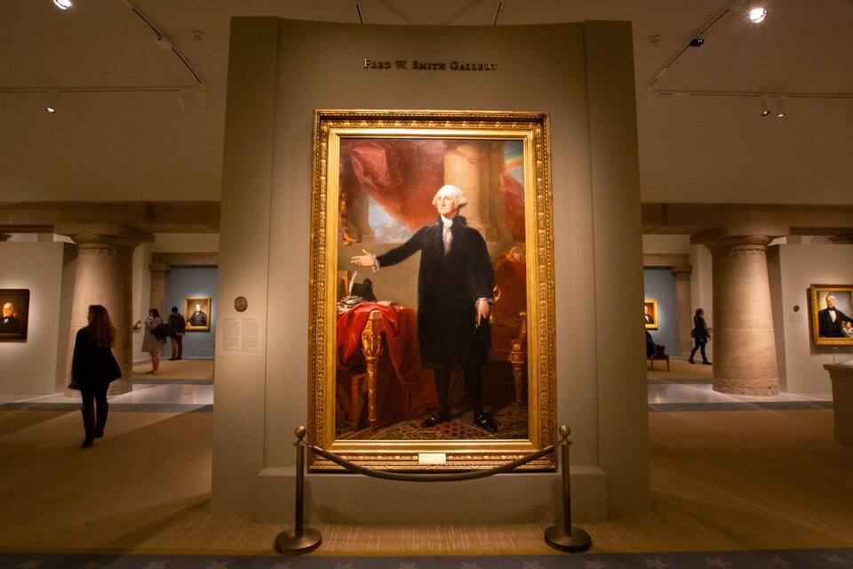 Museu com um grande retrato de uma figura histórica emoldurado em ouro, rodeado por outras obras de arte e visitantes.