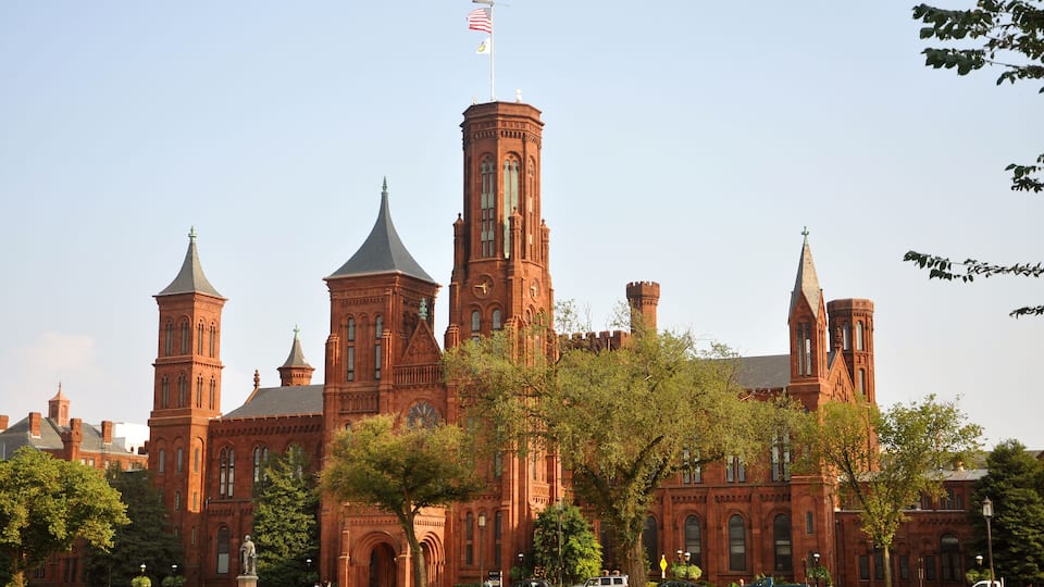 A large red brick building with multiple towers and a flag.