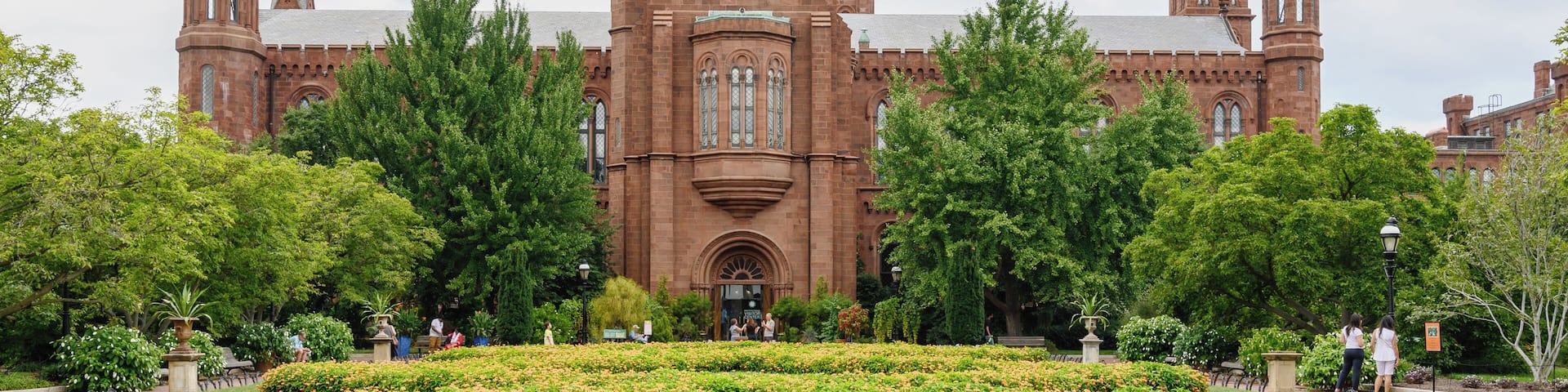 A large brick building with a central tower and two smaller towers, surrounded by well-maintained gardens and trees.