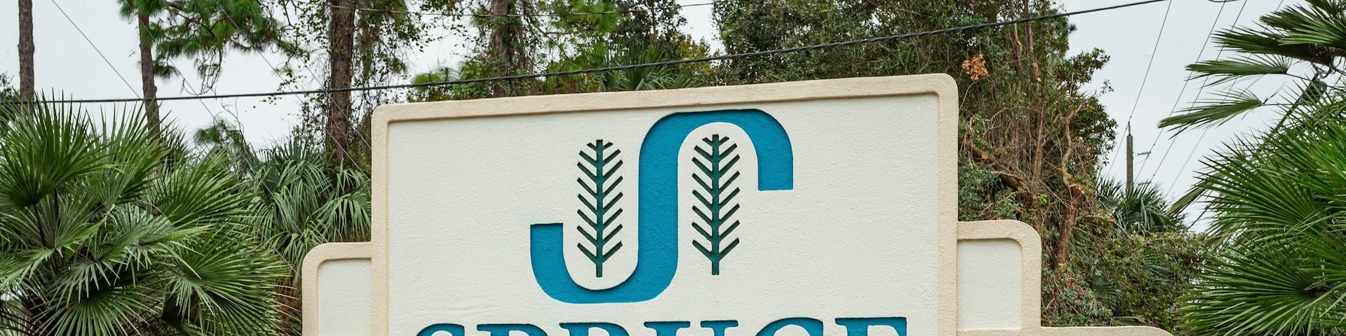 A sign for Spruce Creek, Yely-In Community, surrounded by lush greenery.