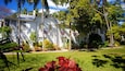 A white house with red and white flags, surrounded by lush greenery and palm trees.