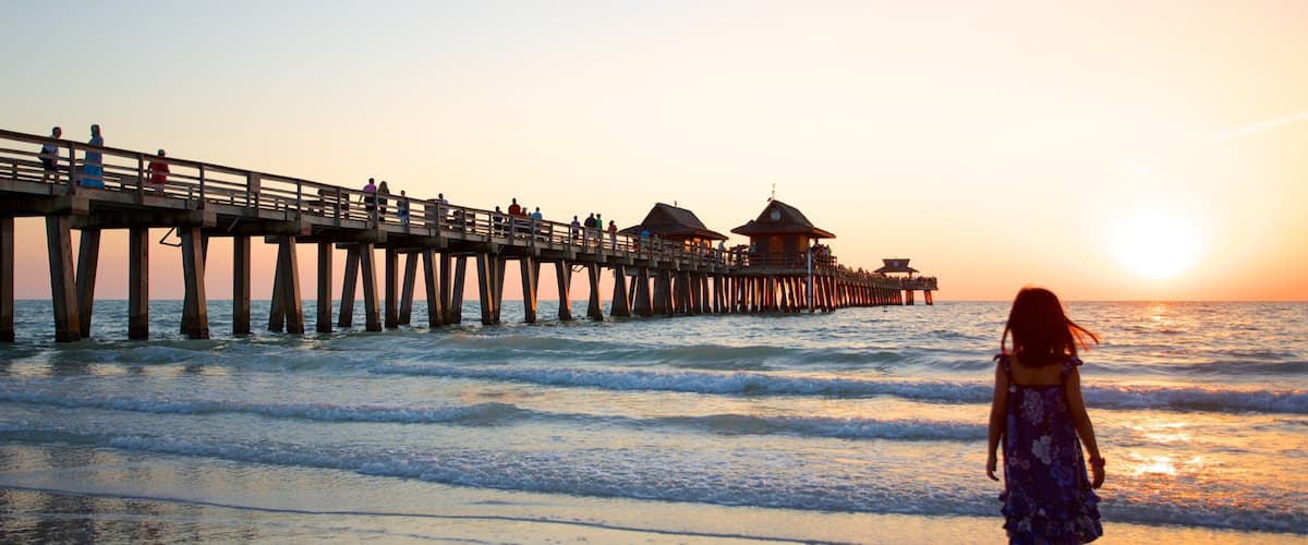 Naples Pier showing a sunset and a beach as well as an individual child