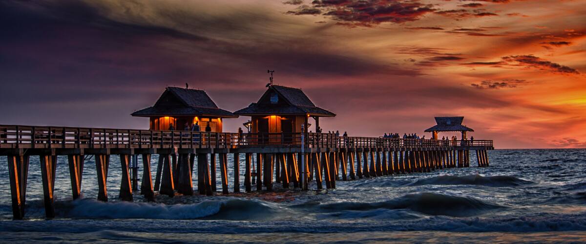 A pier with two illuminated structures and a lookout point extending into the ocean during sunset.