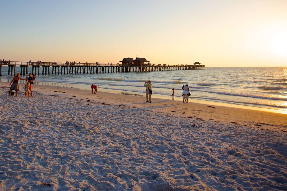 A beach with people walking and a pier extending into the water.