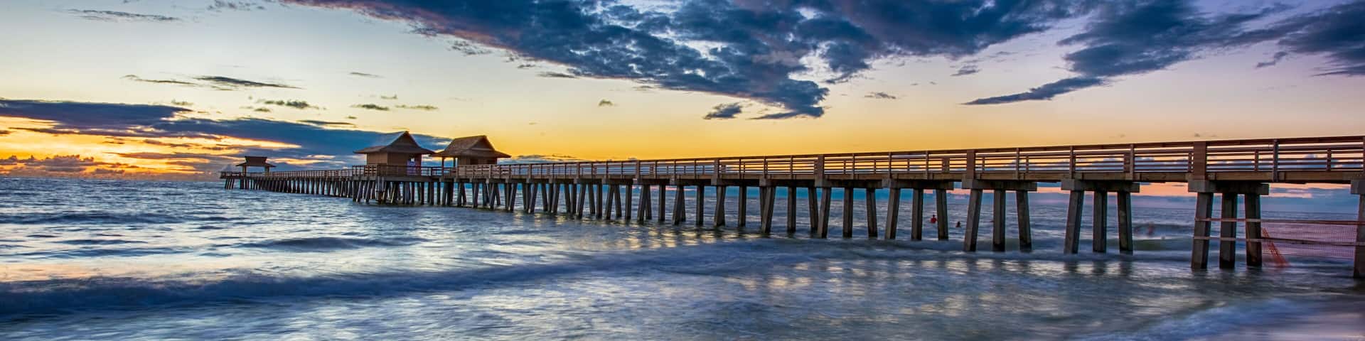 A wooden pier extending into the ocean at sunset with a clear sky and calm water.