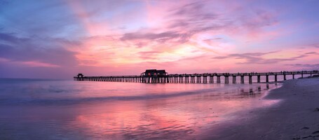 A pier extending into a calm sea at sunset with a beach on the right.