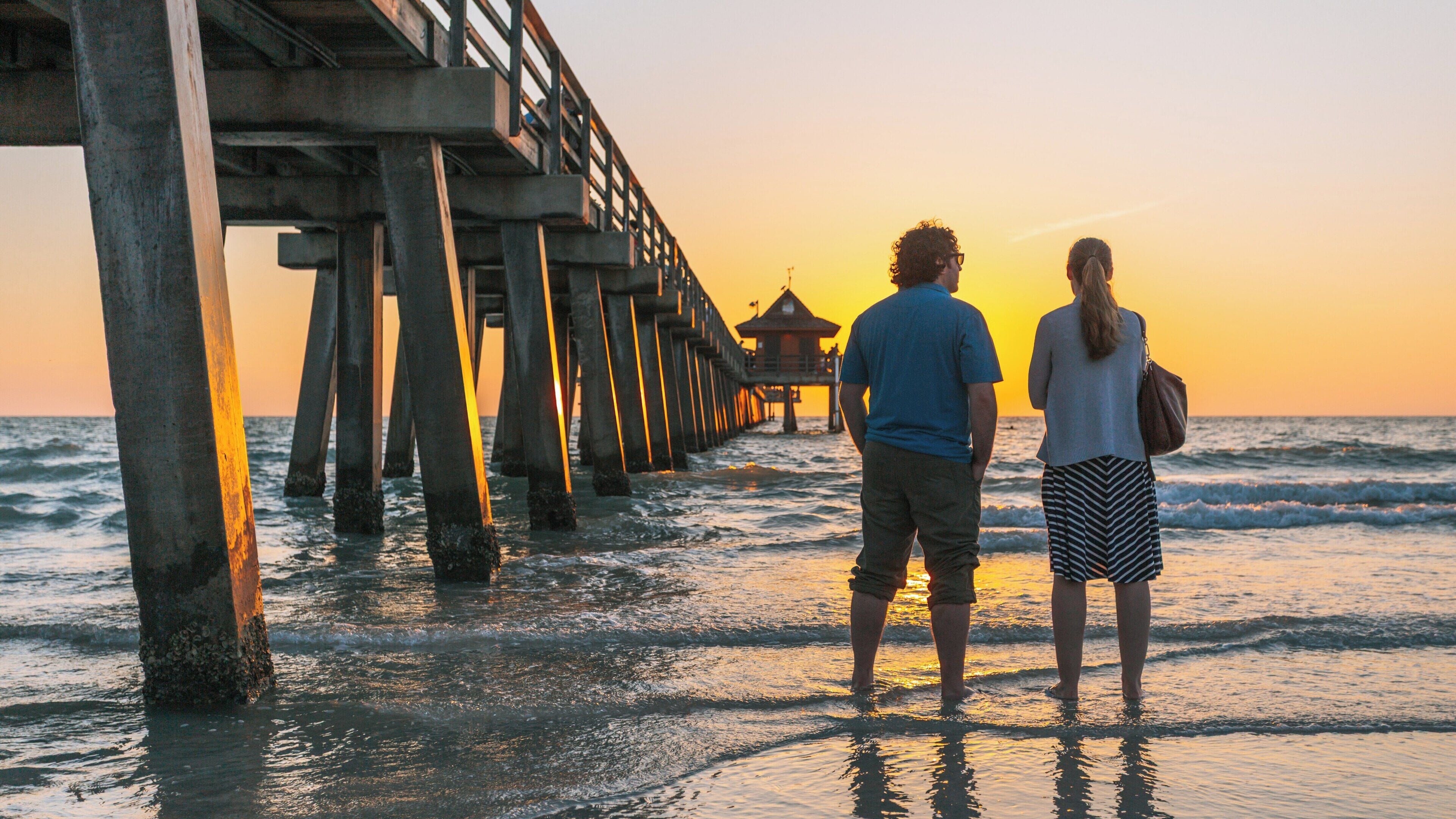 Couple enjoys a sunset stroll at Naples Pier in Old Naples, Florida, with waves lapping at their feet