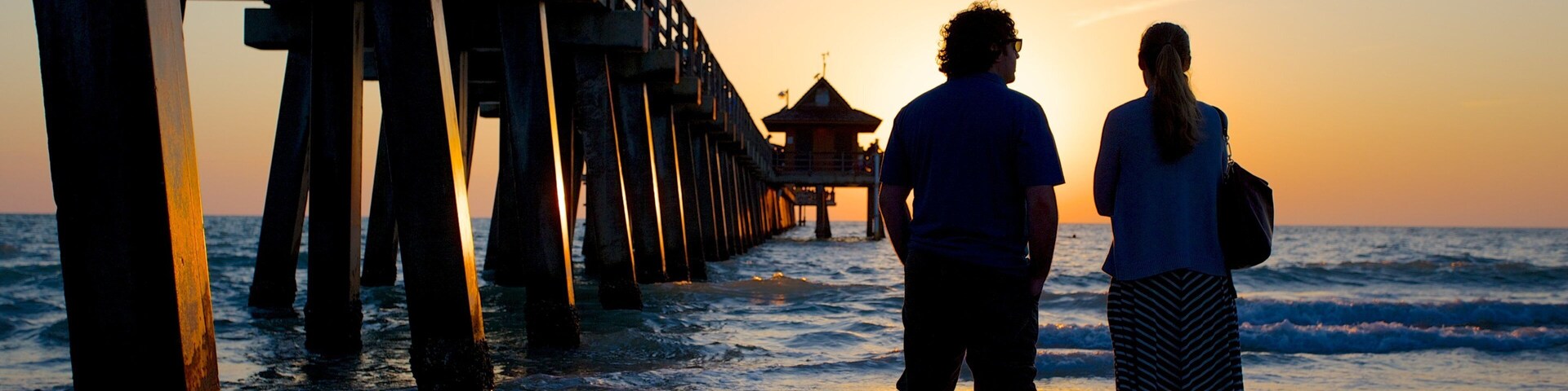 Un muelle que se adentra en el océano al atardecer, con dos personas al final.